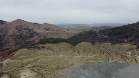 Perspectiva-Aérea-Del-Paisaje-Volcánico-De-Las-Montañas-De-Rumania-Con-Sus-Volcanes-De-Lodo,-Tierra-Seca-Con-Grietas,-Con-Algunas-Casas-Y-Pueblos-Aislados