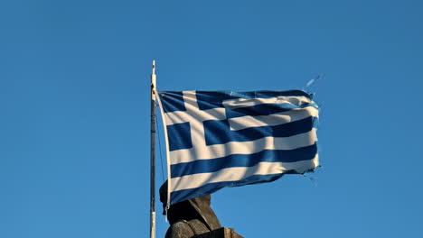 Greek-Flag-Waving-Against-Clear-Blue-Sky-with-Monument-Zagorian-Women-Pindos