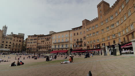 Bustling-main-square-in-Siena,-Italy-with-historic-buildings-and-leisurely-visitors