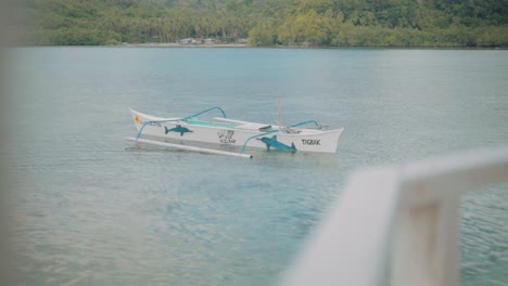 Traditional-Outrigger-Wooden-Boat-Dock-Near-The-Shoreline-Of-A-Blue-Tropical-Beach