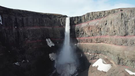 Aerial-pedestal-shot-of-Hengifoss-waterfall-in-East-Iceland,-showcasing-its-red-clay-and-basalt-columns