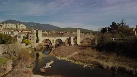 Medieval-bridge-and-river-in-Besalu-town,-Girona,-Spain,-surrounded-by-historic-buildings-and-nature