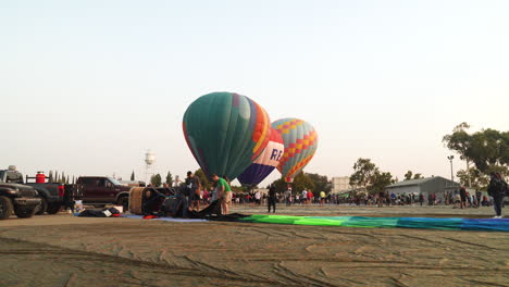 3-Grounded-Hot-Air-Balloons-being-prepped-for-Takeoff-while-a-crew-packs-up-a-deflated-balloon