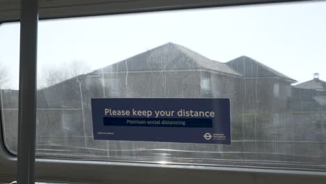 Blick-Auf-Das-Schild-„Bitte-Abstand-Halten“-Am-Fenster-Eines-Fahrenden-Zuges-Der-Jubilee-Line