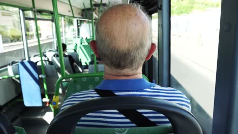 Back-view-of-an-old-man-sitting-on-an-empty-moving-bus-scratching-his-head-at-daytime