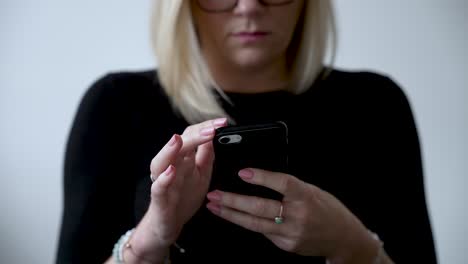 Blonde-woman-typing-on-a-smartphone,-wearing-glasses,-close-up,-indoors