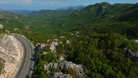 Aerial-view-over-a-road,-revealing-a-valley-in-the-highlands-of-Budva,-Montenegro