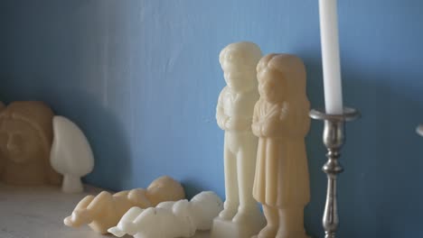 Wachsfiguren-Von-Kindern-Und-Babys-Auf-Einem-Regal-Mit-Blauem-Wandhintergrund-Und-Silbernem-Kerzenständer