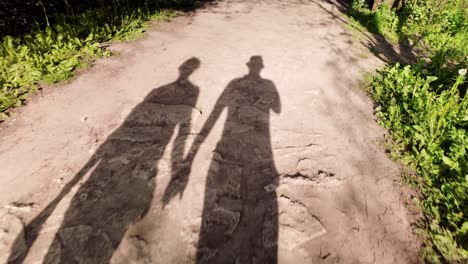 Long-silhouette-shadows-of-couple-walking-along-nature-trail-hand-in-hand