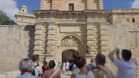 Tourists-pass-through-the-Baroque-portal-of-Mdina-Gate,-also-called-the-Main-Gate-or-Vilhena-Gate,-the-primary-entrance-to-the-fortified-city-of-Mdina,-Malta