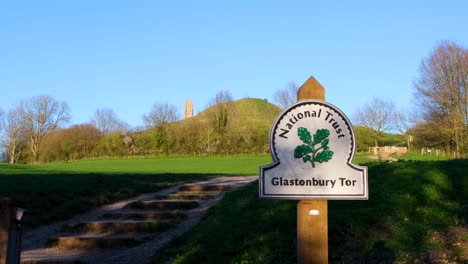 A-view-of-popular-tourism-attraction-of-The-Tor-with-National-Trust-signpost-on-the-Somerset-Levels-in-Glastonbury,-England-UK