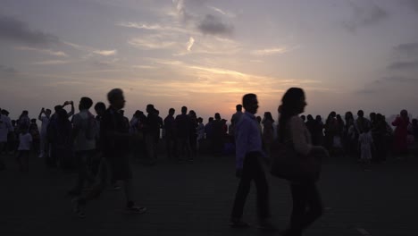 Crowd-of-tourists-enjoying-sunset-at-Marine-Drive-in-South-Mumbai,-Silhoutte-of-people-against-sunlight