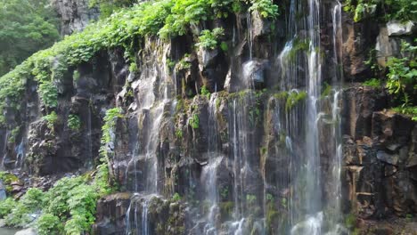 A-mesmerizing-waterfall-cascades-down-rocky-cliffs,-surrounded-by-lush-green-vegetation