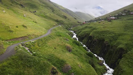 A-picturesque-mountain-road-winds-through-lush-green-valleys-with-a-stream-running-alongside-it