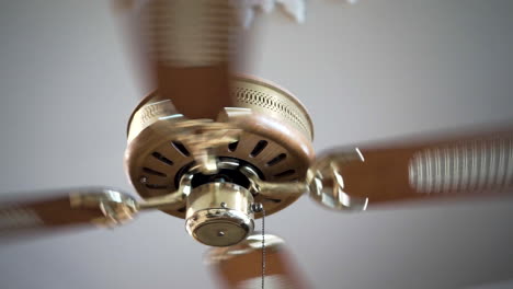 Ceiling-fan-spinning,-wooden-and-gold-decorated,-close-up