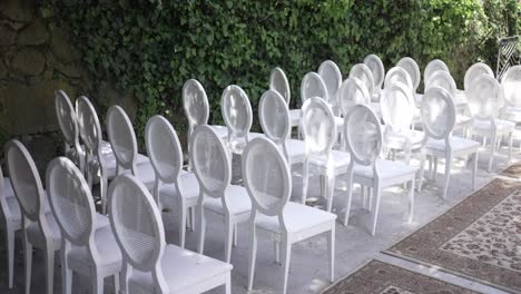 Weiße-Stühle-Für-Eine-Veranstaltung-Im-Freien-Vor-Einer-Efeubewachsenen-Steinmauer