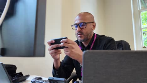 Portrait-Of-A-Bald-Man-With-Eyeglasses-Using-Smartphone-Inside-The-Workplace