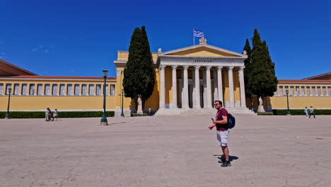 Man-with-bagpack-stands-in-front-of-Zappeion-Hall,-neoclassical-building-in-Athens,-Greece,