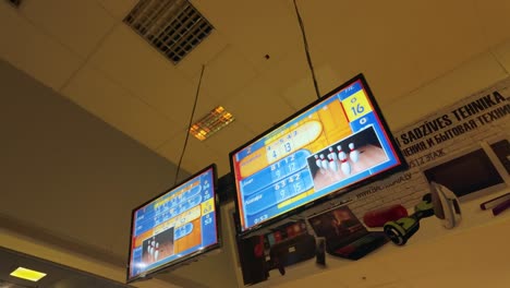 Footage-shows-TV-screens-in-a-bustling-bowling-venue,-displaying-live-game-scores-and-player-results