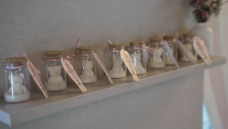 Reihe-Von-Kleinen-Gläsern-Mit-Teddybär-Kerzen-Auf-Einem-Regal,-Dekoriert-Mit-Rosa-Bändern