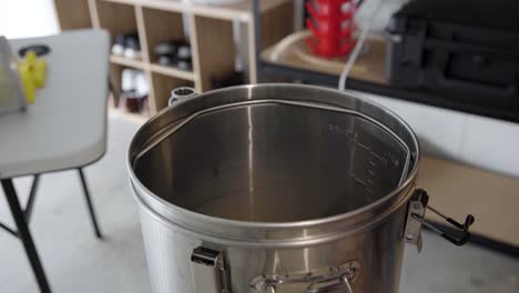 Inserting-false-bottom-metal-screen-and-mash-tun-into-metal-brewing-kettle,-high-angle-close-up