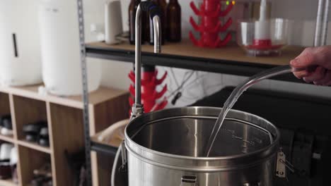 Water-pouring-into-and-filling-up-a-metal-pot-in-a-home-beer-brewing-setup,-close-up