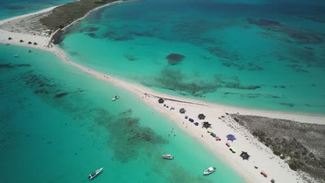 A-tropical-beach-with-turquoise-waters,-boats,-and-sun-umbrellas,-aerial-view
