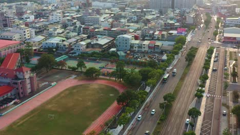 Aerial-view-drone-flyover-capturing-street-traffic-on-Mingde-N-Rd,-Douliu-cityscape-featuring-Gongcheng-Elementary-School-at-sunset
