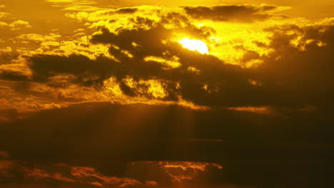 Sun's-rays-pierce-through-dark-clouds,-casting-a-golden-glow-in-time-lapse