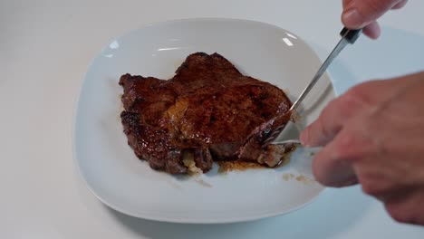 High-angle-shot-of-medium-cooked-entrecote-on-a-white-plate,-cut-with-fork-and-knife-to-show-juicy-meat