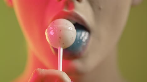 Young-woman-with-blue-tongue-licks-white-lollipop,-focus-rack-close-up-face