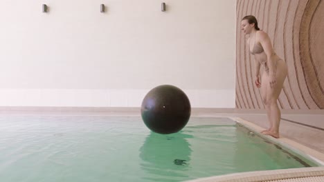 Caucasian-woman-leaps-and-fails-to-land-on-floating-exercise-ball-in-pool,-slomo