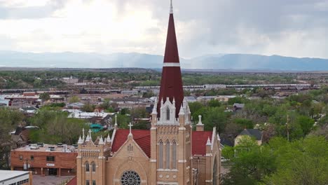 Drone-ascends-front-of-arched-windows-along-tower-spire-to-cross-of-cathedral-in-Pueblo-Colorado
