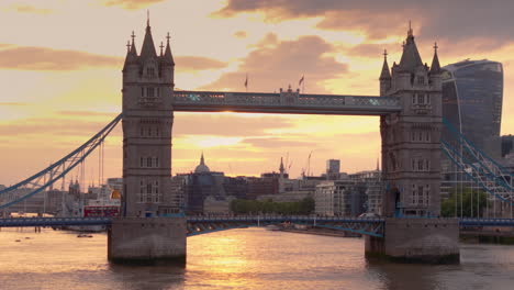 London-bus-cross-iconic-Tower-Bridge-against-fiery-sunset-sky,-telephoto-aerial