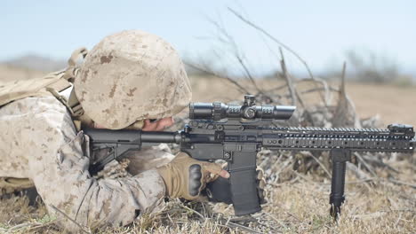 SLOW-MOTION:-A-US-Marine-positioned-in-the-desert-takes-aim-with-his-assault-rifle-while-laying-down-and-adjusts-scope