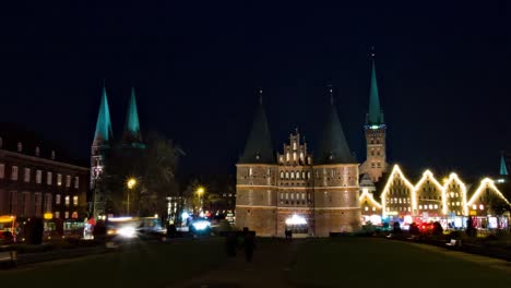 Panning-time-lapse-of-Museum-Holstentor-western-gate-in-Lübeck,-Germany,-at-night-with-churches-in-the-background