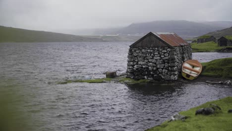 Weite-Aufnahme-Eines-Alten-Verlassenen-Steingebäudes-Am-Ufer-Eines-Natürlichen-Sees-An-Bewölkten-Tagen-Auf-Den-Färöer-Inseln