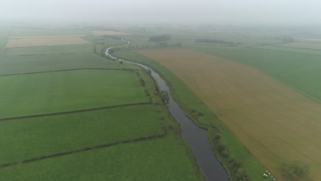 Aerial-shot-above-farmlands-and-the-river-Forth,-following-the-river-on-a-misty-day