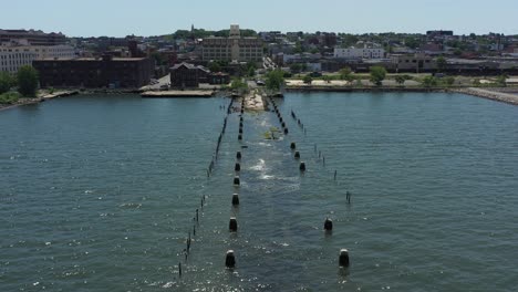 low-flying-drone-shot-over-an-old,-partly-sunken,-abandoned-pier,-with-the-sun-shinning---shimmering-onto-the-waters-below