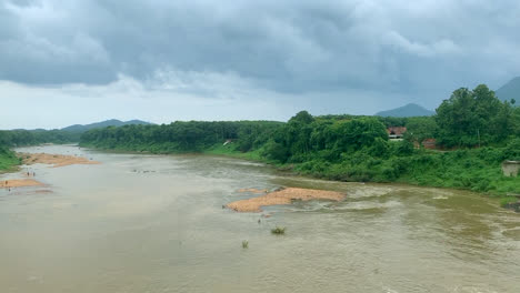 Un-Hermoso-Paisaje-De-Un-Lago-Que-Fluye-Después-De-Una-Lluvia-En-Kerala-Con-Montañas-Y-Zonas-Verdes-Al-Fondo