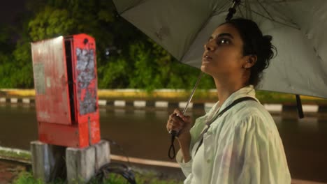 Woman-holding-an-umbrella-on-a-rainy-night-waiting-by-the-roadside